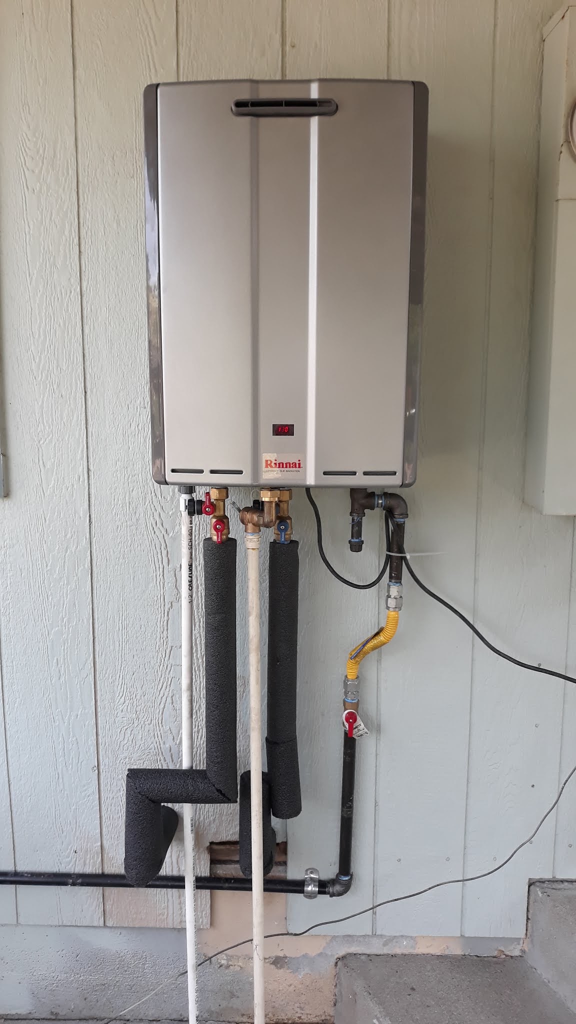 A finished tankless gas water heater installation on an exterior wall
