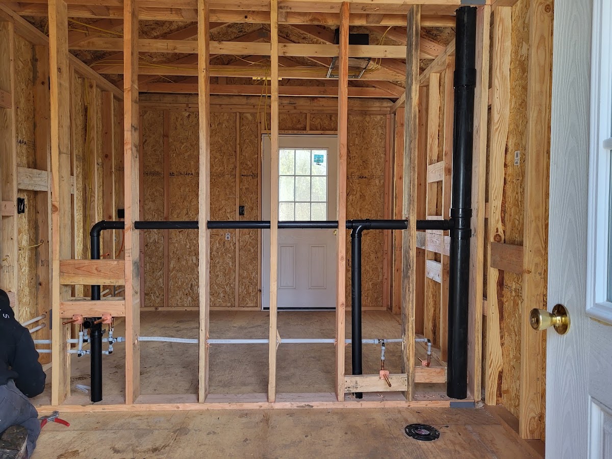A plumber working on rough-in piping inside a framed room under construction